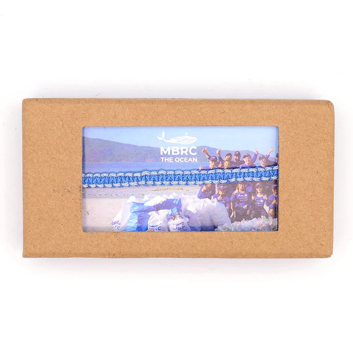 Das MBRC-Armband besteht aus recycelten Meeresmaterialien und wird in einer eleganten Pappschachtel mit einem Foto einer Strandsäuberung geliefert, um das Engagement des Unternehmens zur Reduzierung von Plastikmüll in den Ozeanen und zum Erhalt der natürlichen Schönheit zu demonstrieren.
