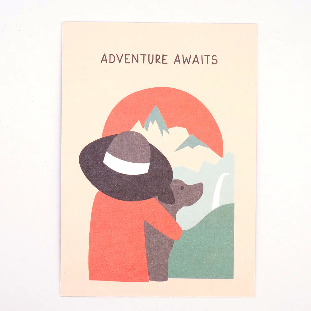Das 3er-Set Postkarten von Roadtyping ist die perfekte Ergänzung für Ihre Sammlung zum Thema Reisen und zeigt eine Illustration einer Person und eines Hundes, die Berge bestaunen, mit dem Text „Das Abenteuer wartet“.
