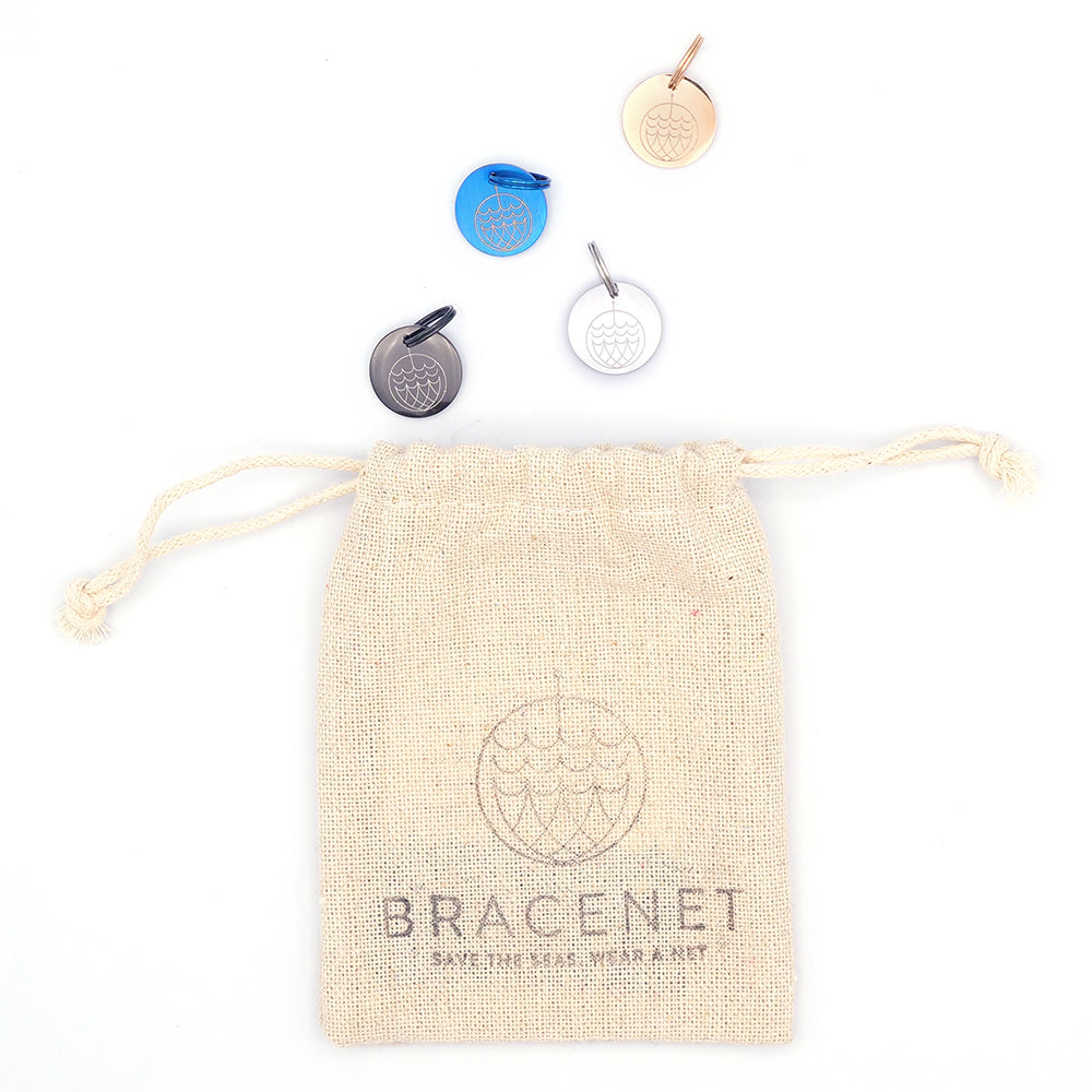 Über einem Bracenet-Kordelzugbeutel prangen darüber vier Anhänger Maritim von Bracenet in Blau, Schwarz, Silber und Beige.