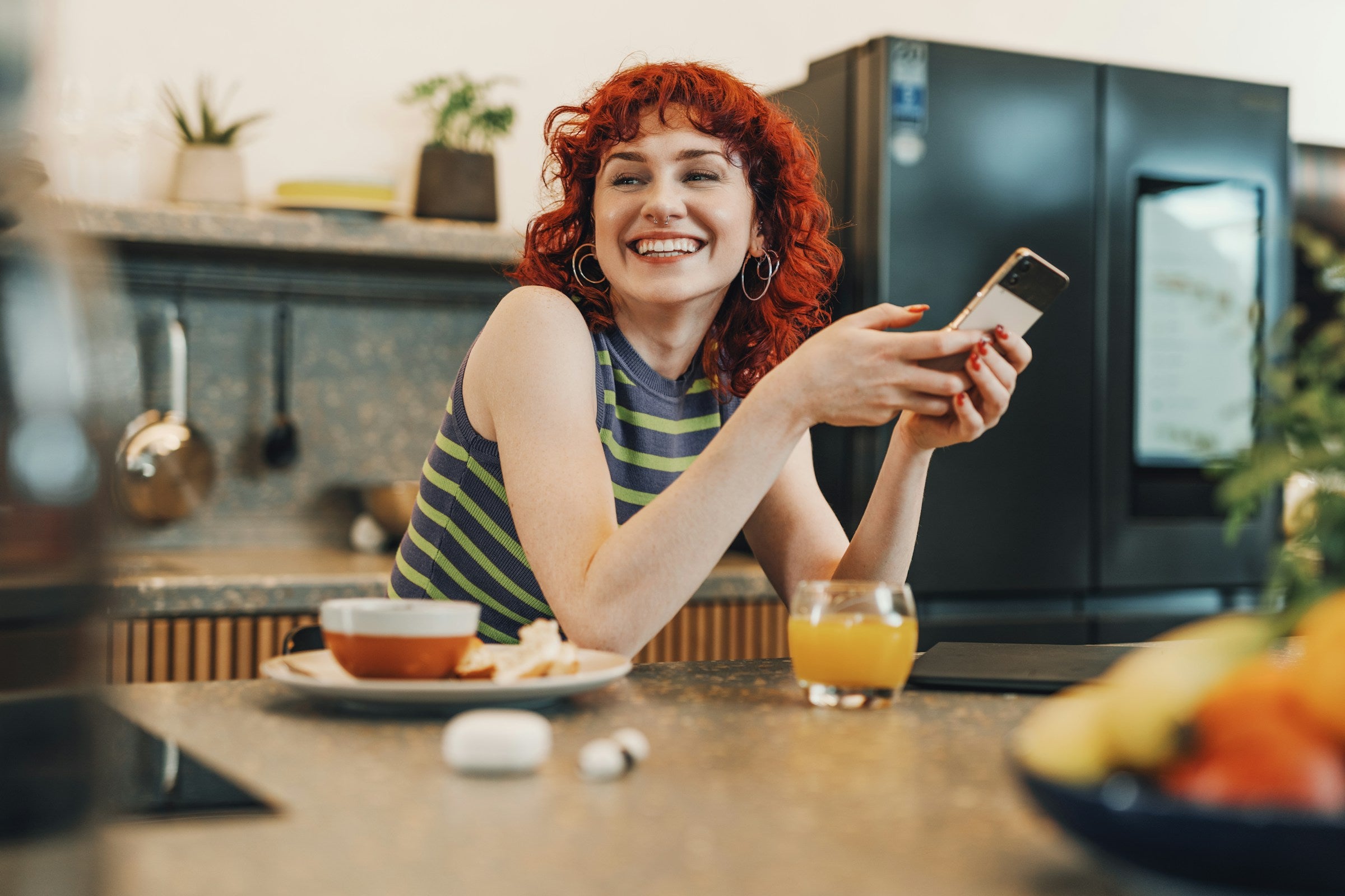 Frau sitzt in Küche mit Smartphone